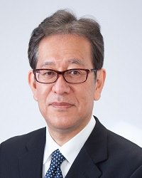 スーツと眼鏡の男性がシンプルな背景の前に立っています。