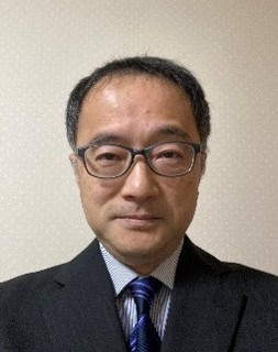 メガネとスーツの男性がカメラを見て微笑んでいます。