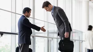 廊下でビジネスマンが握手とお辞儀をして挨拶している。