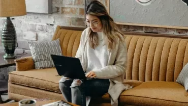 Person using a laptop on a brown couch in a cozy living room.