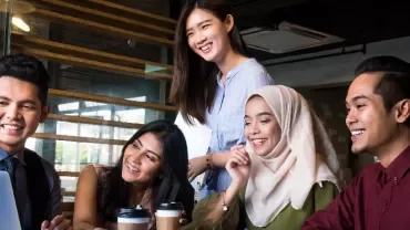 Group of five people smiling while looking at a laptop.