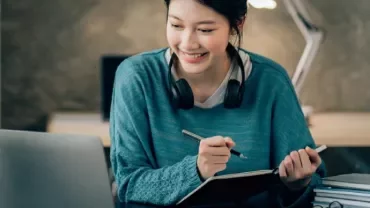 ノートパソコンとノートを使って勉強している女性。