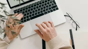 Person working on a laptop with notepad and glasses nearby
