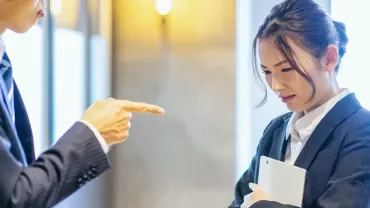 スーツを着た男性がオフィスでタブレットを持つ女性を指している。