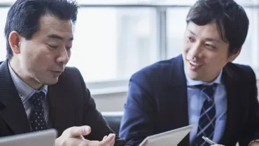 スーツを着た2人のビジネスマンが会議用テーブルで議論している。