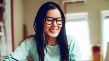 眼鏡をかけた女性がコンピュータを見ながら微笑んでいる。