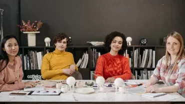 本棚を背景にテーブルに座る4人の人々。