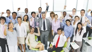 明るいオフィスで大勢の多様なオフィスワーカーが喜んでいる様子。