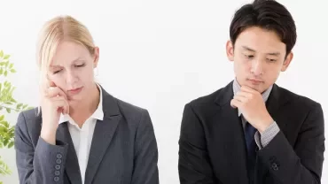 ビジネススーツの男女が考え込んでいる様子。そばに観葉植物。