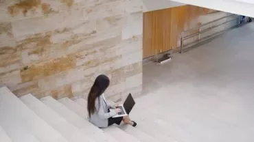 A woman using her laptop while sitting on a staircase, appearing engaged in her work.