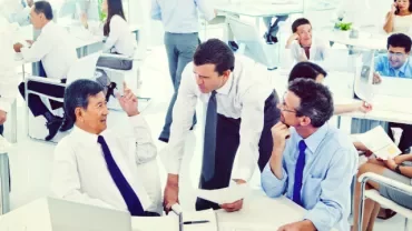 開放的なオフィススペースで同僚が仕事の話し合いをしています。