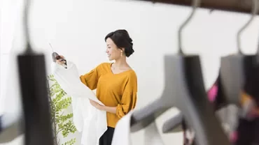 オレンジ色のトップを着た女性がラックから服を選んでいます。