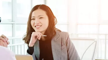 Two people in a bright office, one smiling while holding a pen.