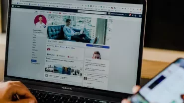 Person using laptop with social media profile and smartphone.