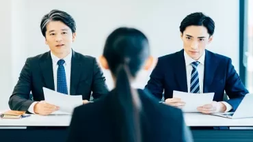2人の男性が机を挟んで面接し、書類を持っている様子。