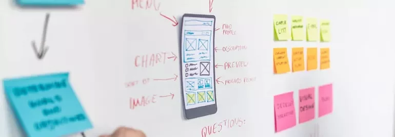 Person planning app design with sticky notes and whiteboard sketches.