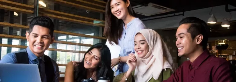 Group of five people smiling while looking at a laptop.