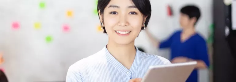 タブレットを持って微笑む人物、背景にカラフルな付箋。