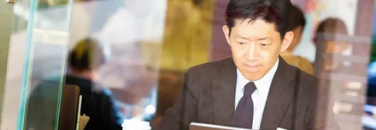 カフェでタブレットを使うスーツ姿の男性。テーブルにはコーヒーカップ。