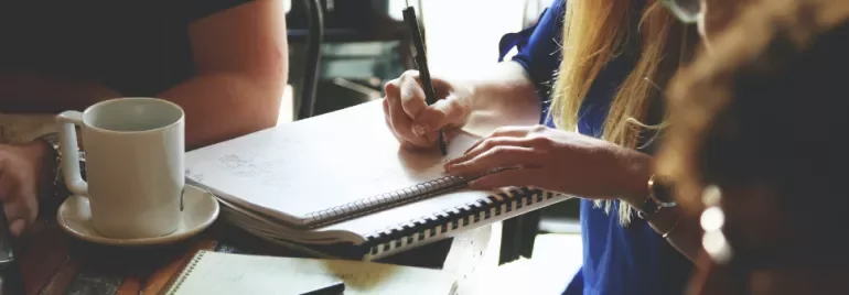 People writing in notebooks and drinking coffee at a table.