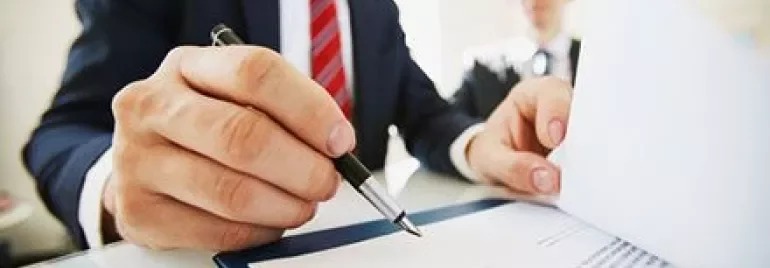 書類に署名する男性と、背景にもう一人の人物。