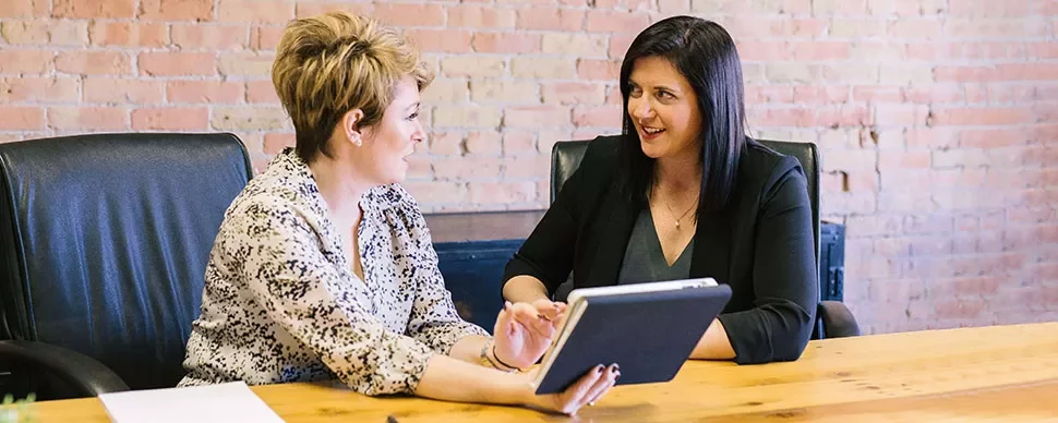 Two women discussing with a tablet at a conference table.