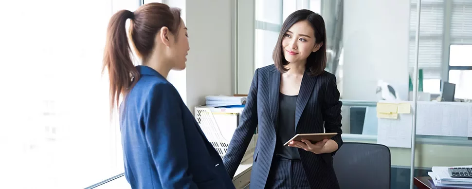 Two women in business attire talking in an office.