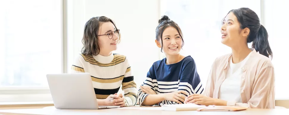 会議室で笑いながら話す三人の女性。