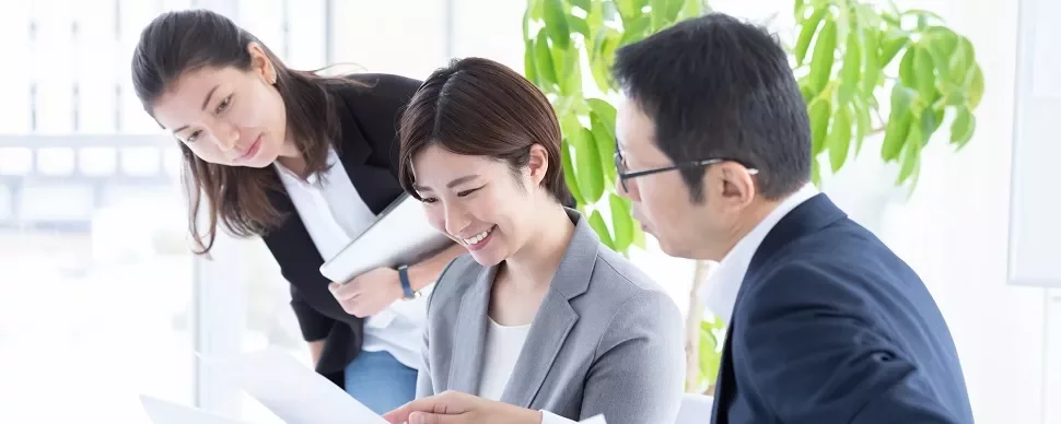 書類を見ながら会議している3人のビジネスパーソン。