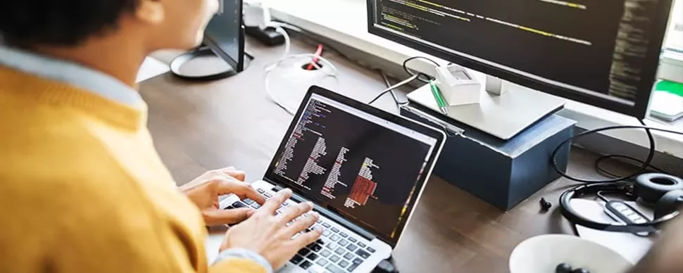 ノートパソコンでコーディングをしている人物とモニター。