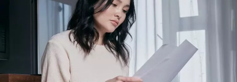 窓辺で書類を読む人、薄いセーターを着ている。