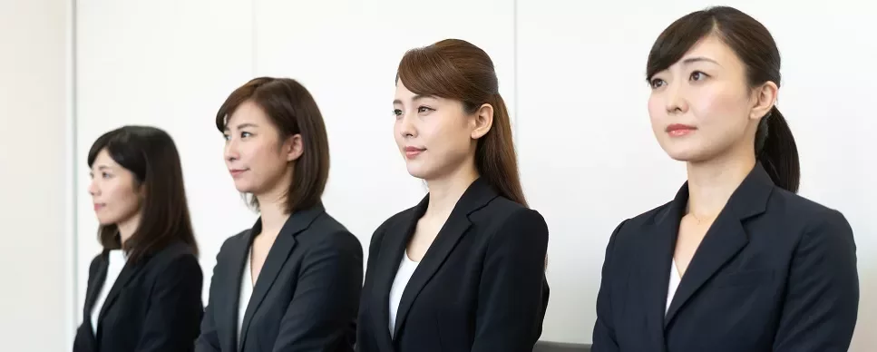 スーツを着た4人の女性が並んで座っています。