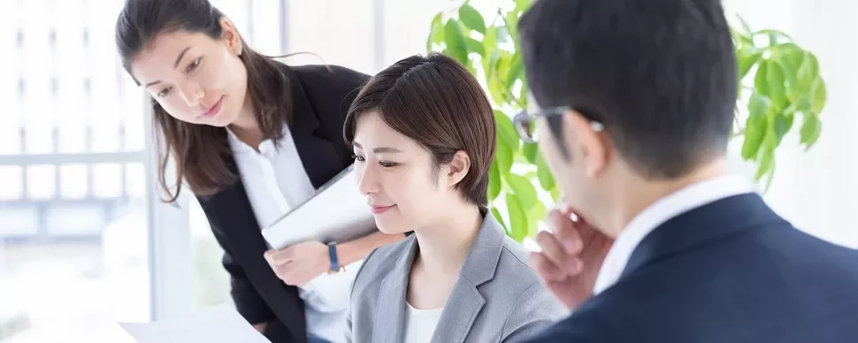 明るいオフィスで書類を確認する3人の同僚。