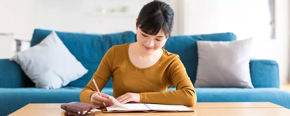 居間でテーブルに座って書き物をする女性。