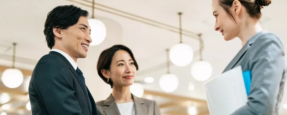 オフィスで会話するビジネススーツ姿の3人。