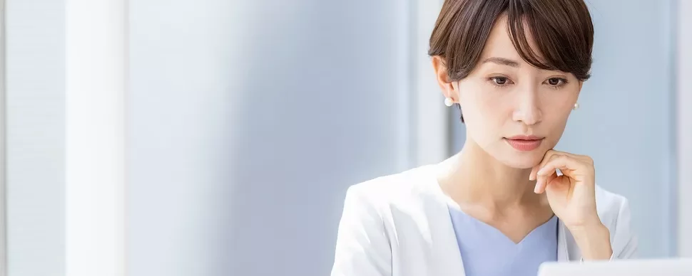 白いブレザーを着た女性がノートパソコンで仕事をしている