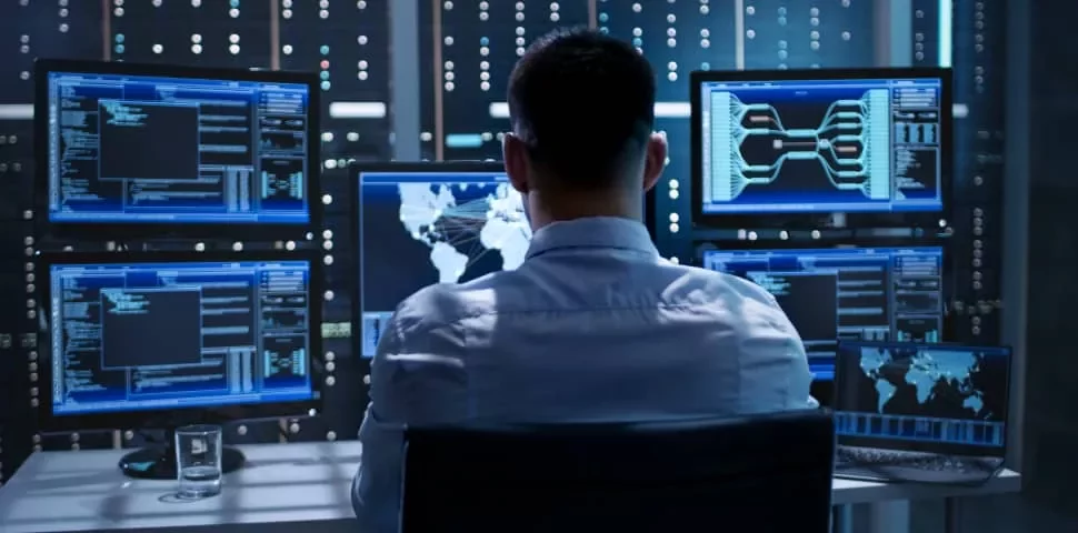 複数のコンピュータ画面でデータを監視する人物。