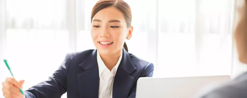 スーツを着た女性が微笑んで、ノートを取っている。