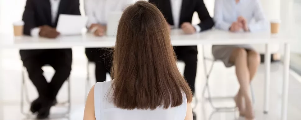 女性がテーブルの面接官と向き合って座っている。