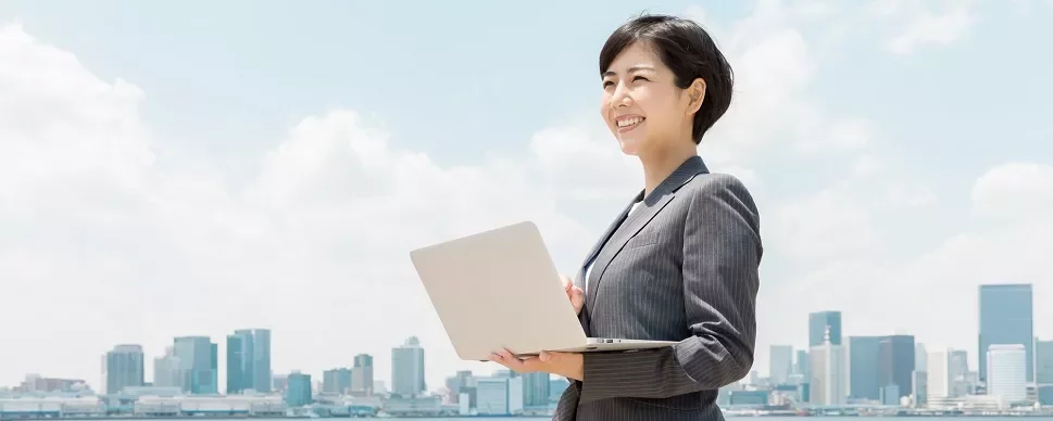 都市の背景を背にノートパソコンを持ったビジネススーツの女性。