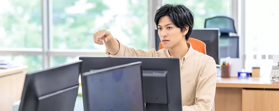 デスクで複数のモニターを使って作業する男性。