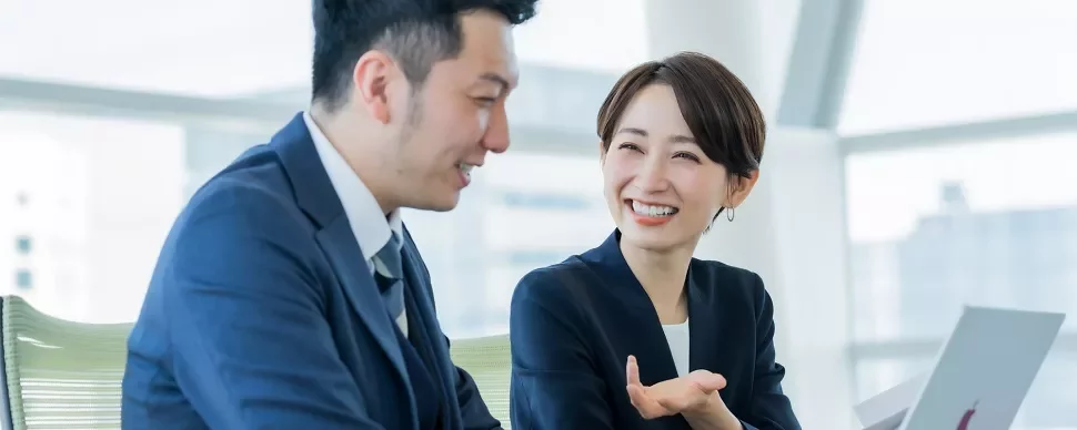 オフィスで笑顔で話すビジネススーツの二人。
