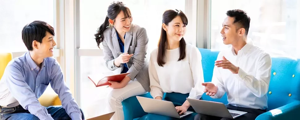 オフィスでノートパソコンを使って話し合う4人の同僚。