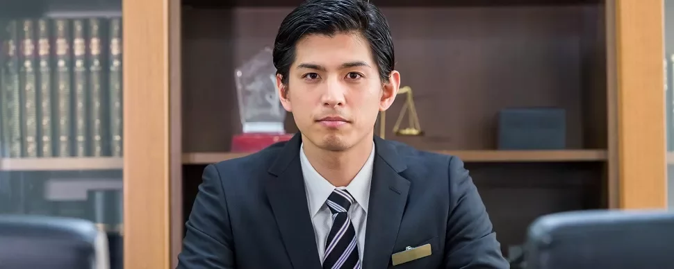 スーツを着た男性が机に座っているシーン。