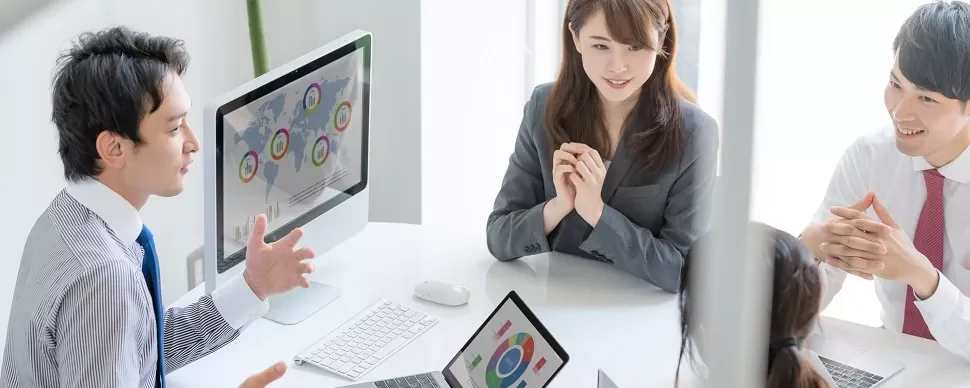 業務会議で、コンピュータ画面のチャートについて話し合う人々。