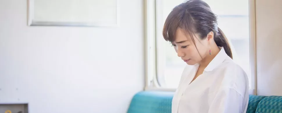 電車の窓際に座る白いシャツの女性。