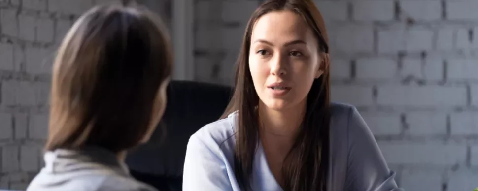 Two women having a serious conversation in an office setting.