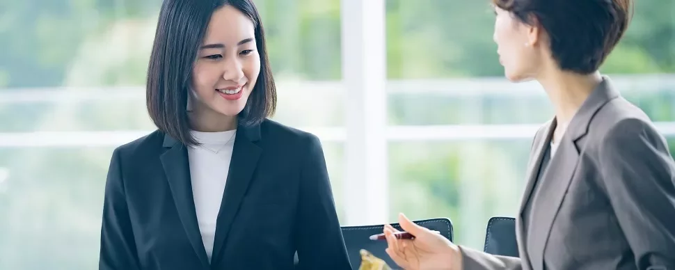 オフィスで話し合うビジネススーツ姿の2人の女性。