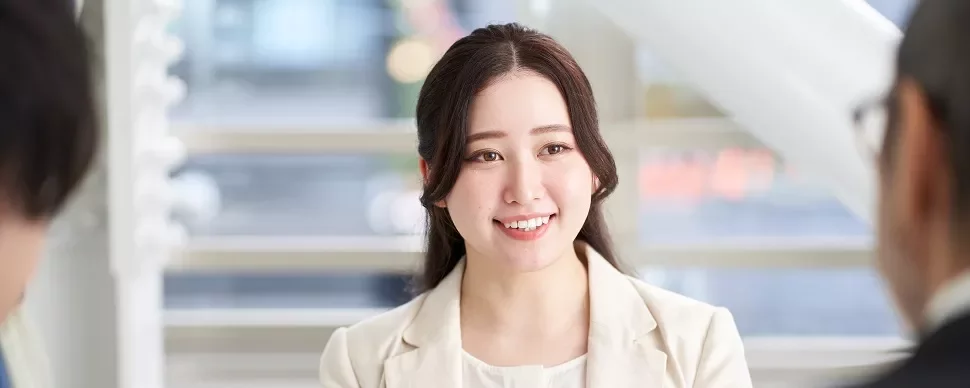 オフィスで2人と話す、笑顔の白いスーツを着た女性