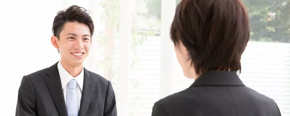 Two people in suits having a conversation in a bright room.